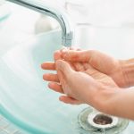 Woman's hands under running water at sink