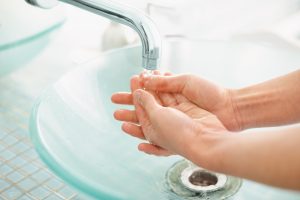 Woman's hands under running water at sink